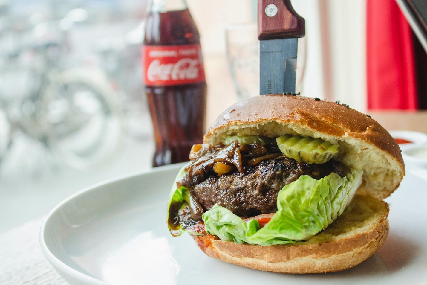 um hambúrguer com salada e carne num prato e uma refrigerante ao lado